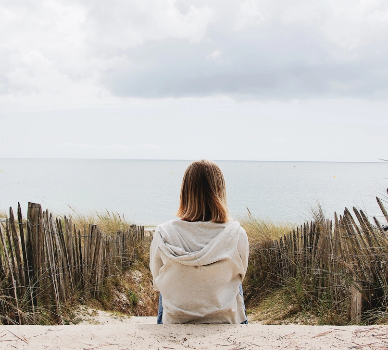 Woman sitting by herself on a beach over the water Woman sitting by herself on a beach over the water